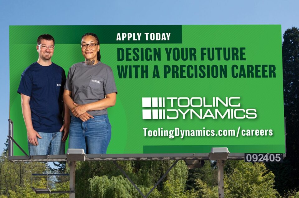 Billboard with two people on a green background. Text reads: Design your future with a precision career. Apply Now. Tooling Dynamics"