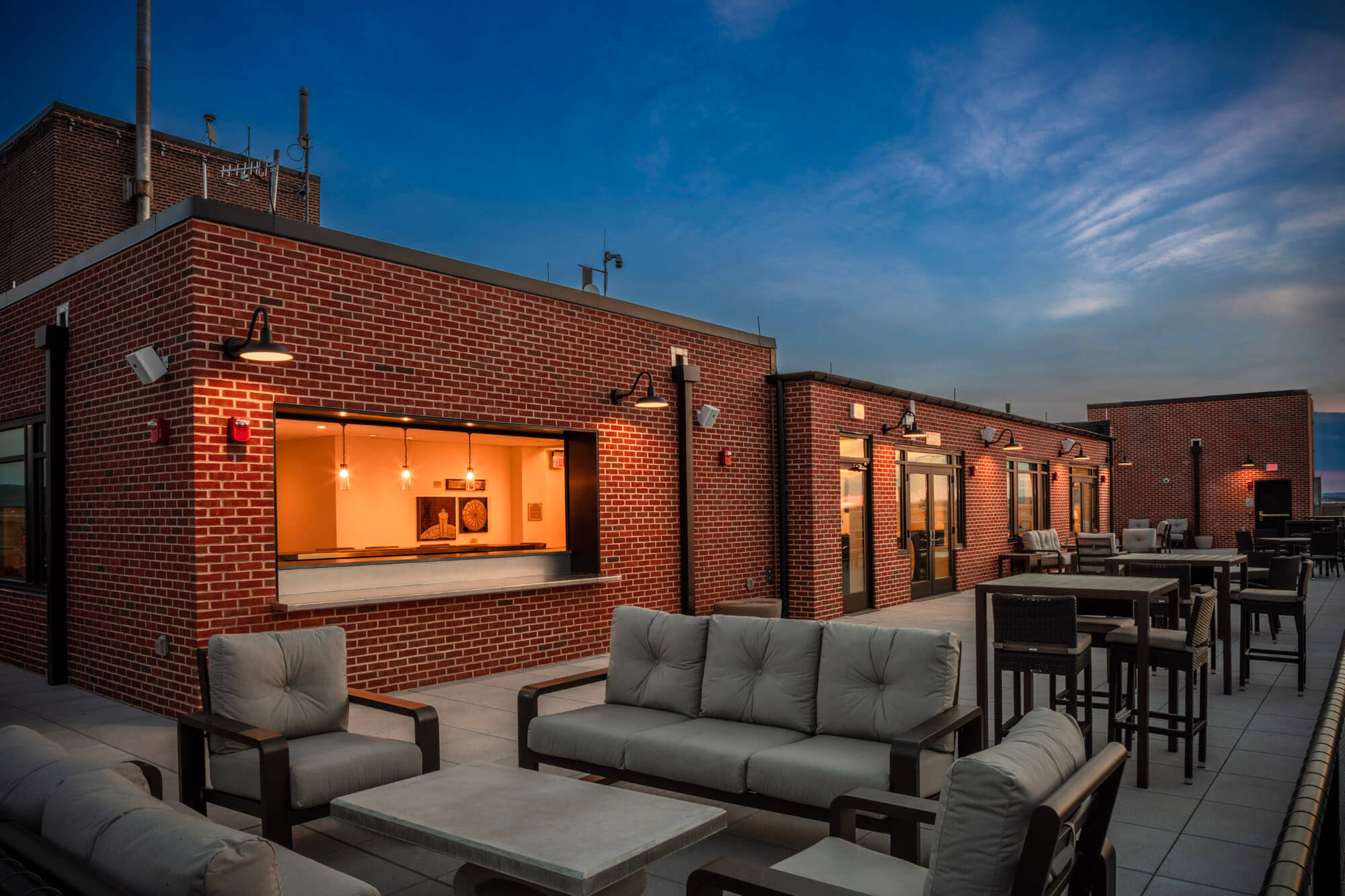 Rooftop bar at the Yorktowne at twilight. The bar is lit up and there are tables and sofas set up.