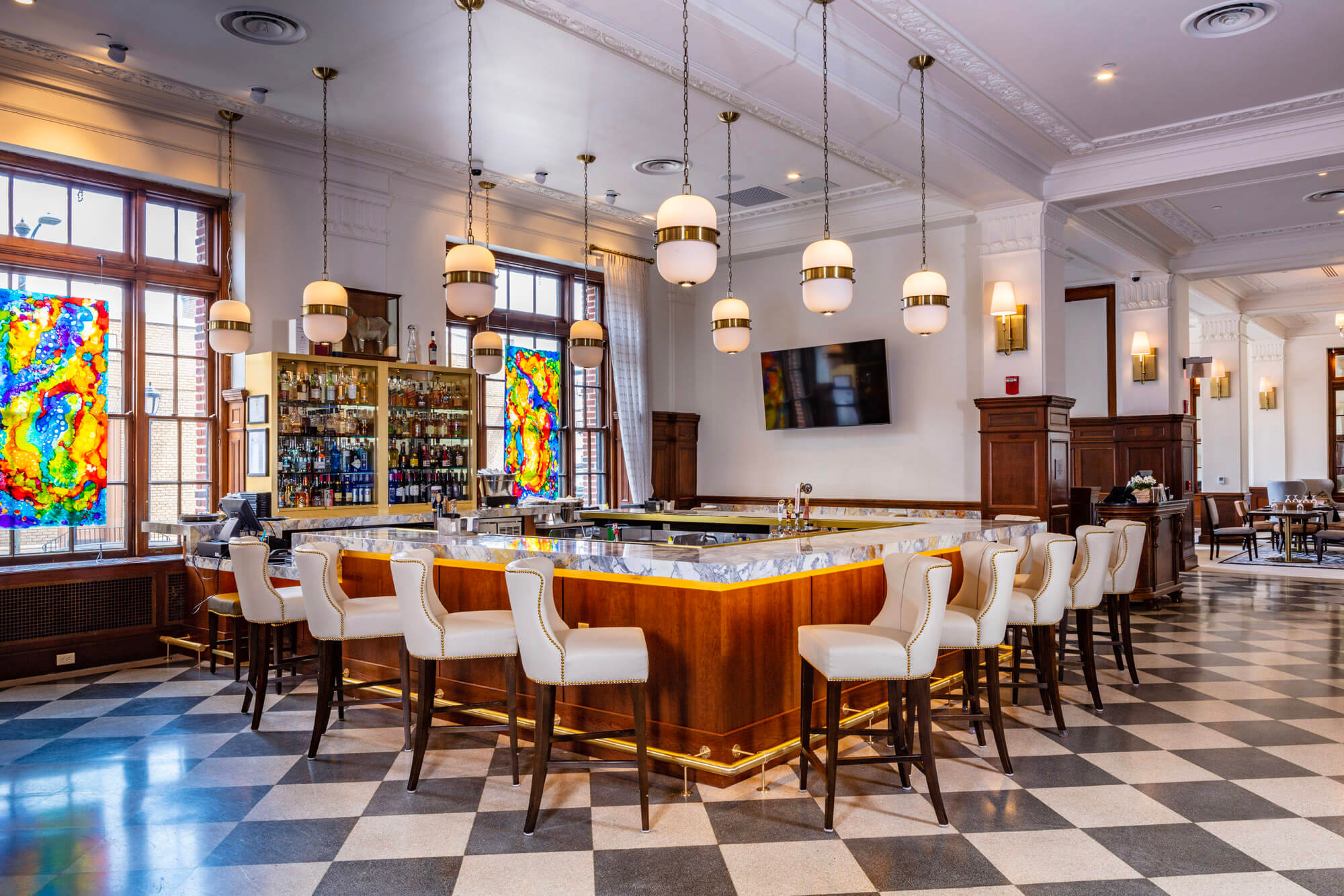 The bar area with low hanging lights, marble bar top, and leather bar stools lining the bar.