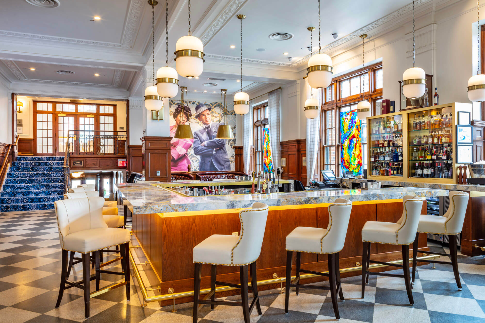 View across the bar with leather bar stools lining the bar and a bright painting in the background.