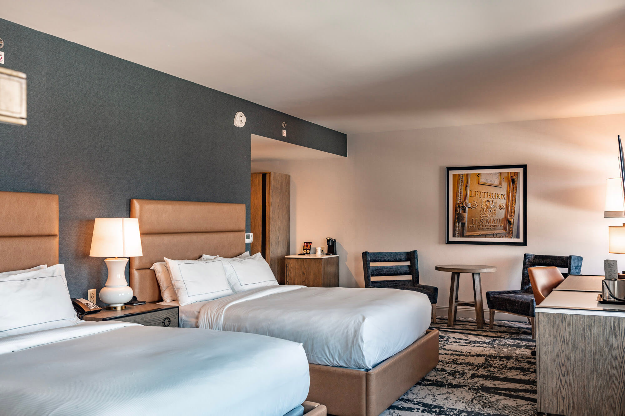 A hotel room with two freshly made beds, a table and chairs, and a small work desk.