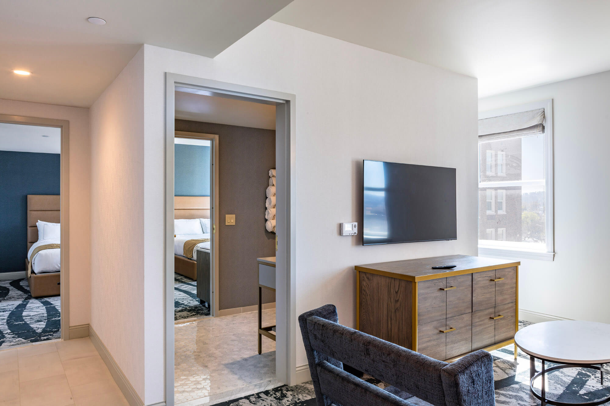 A hotel room with sitting area in the foreground, a bathroom in the middle and a bedroom in the distance.