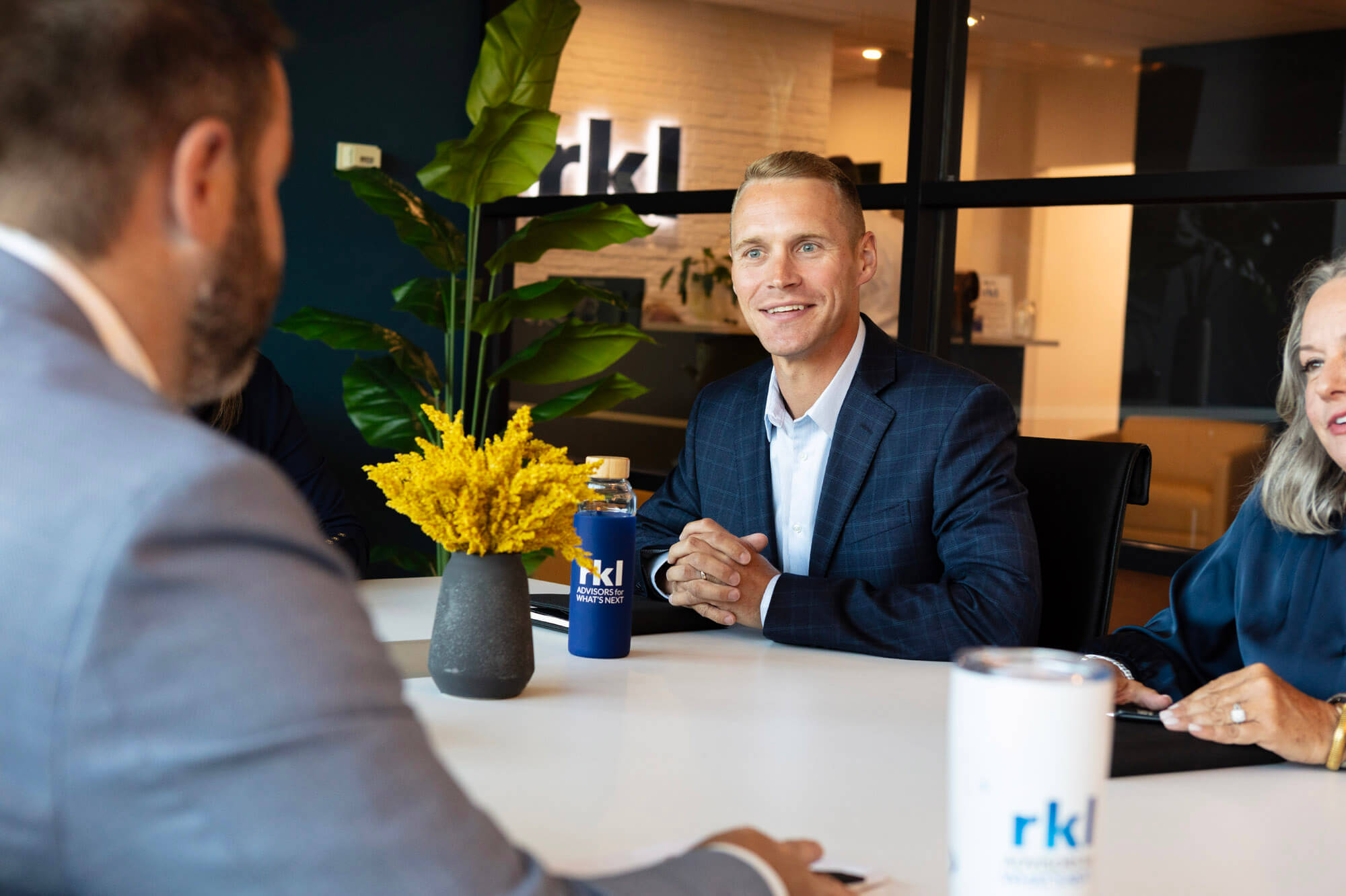 Three people sitting at a desk with notes and RKL branded coffee cups.