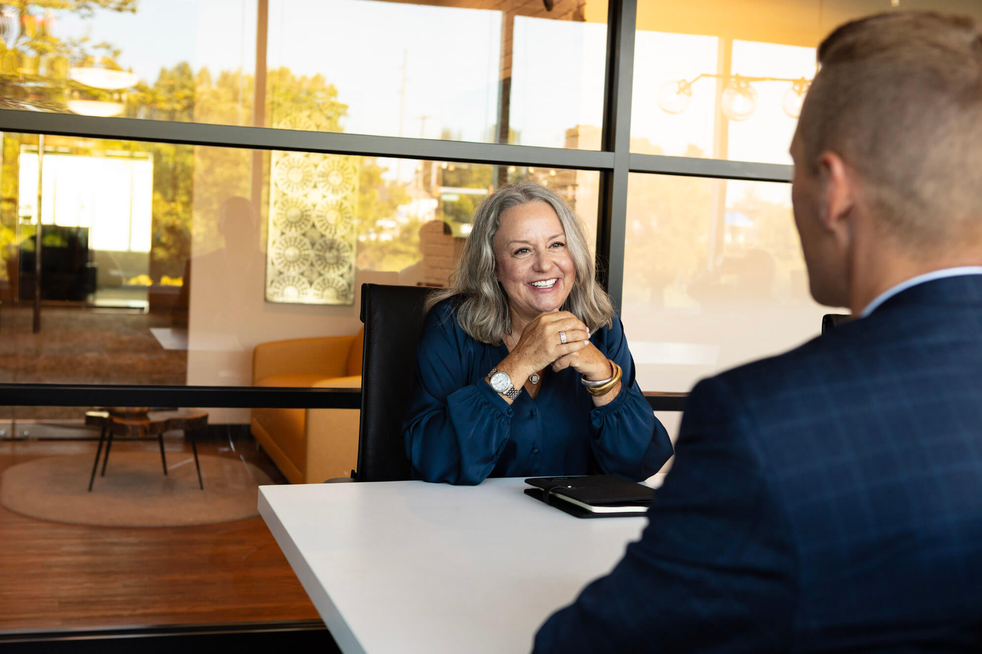 A lady smiling and talking to a man on the other side of the conference table.