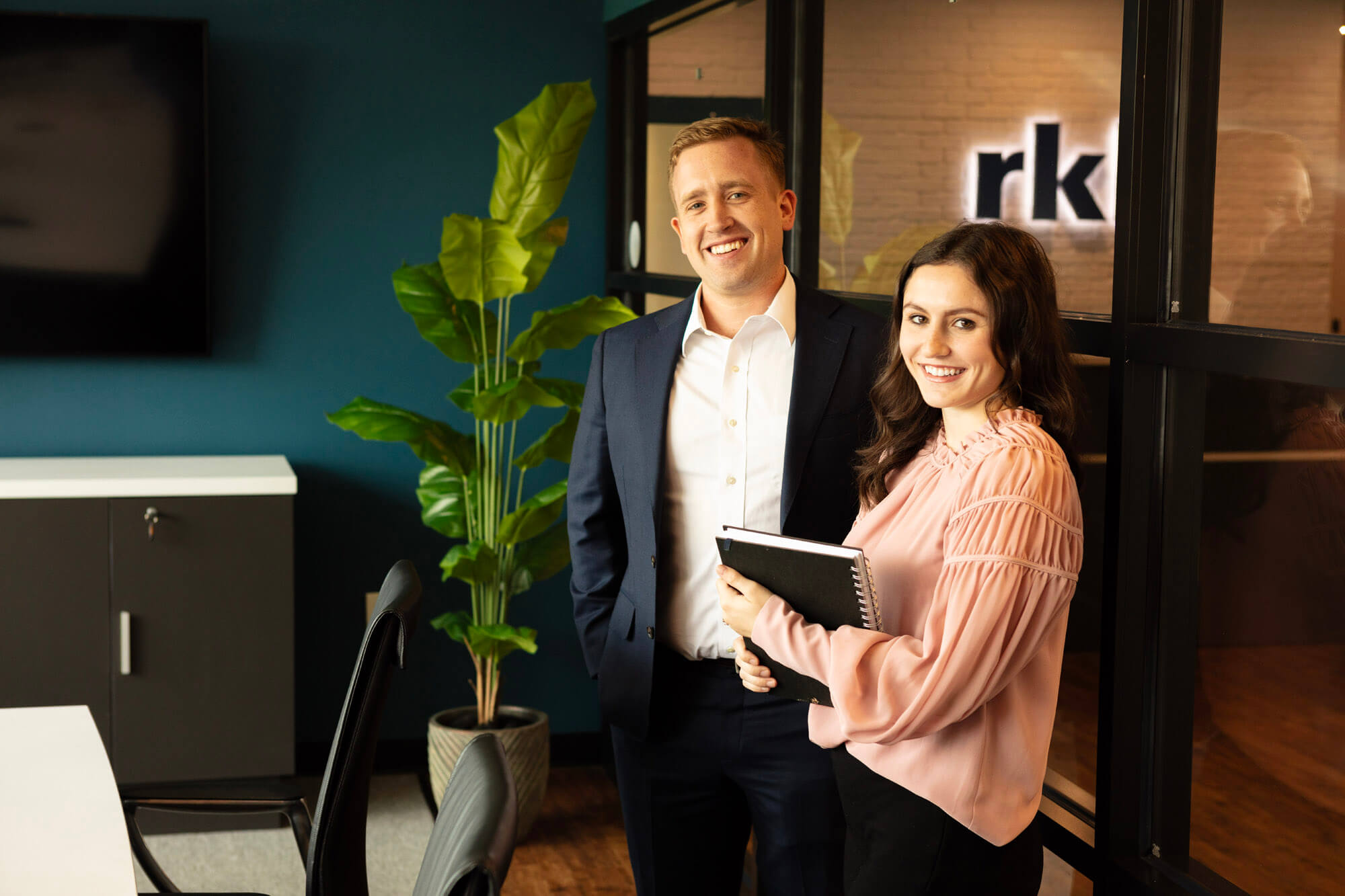 A man and woman smiling at the camera in an office.