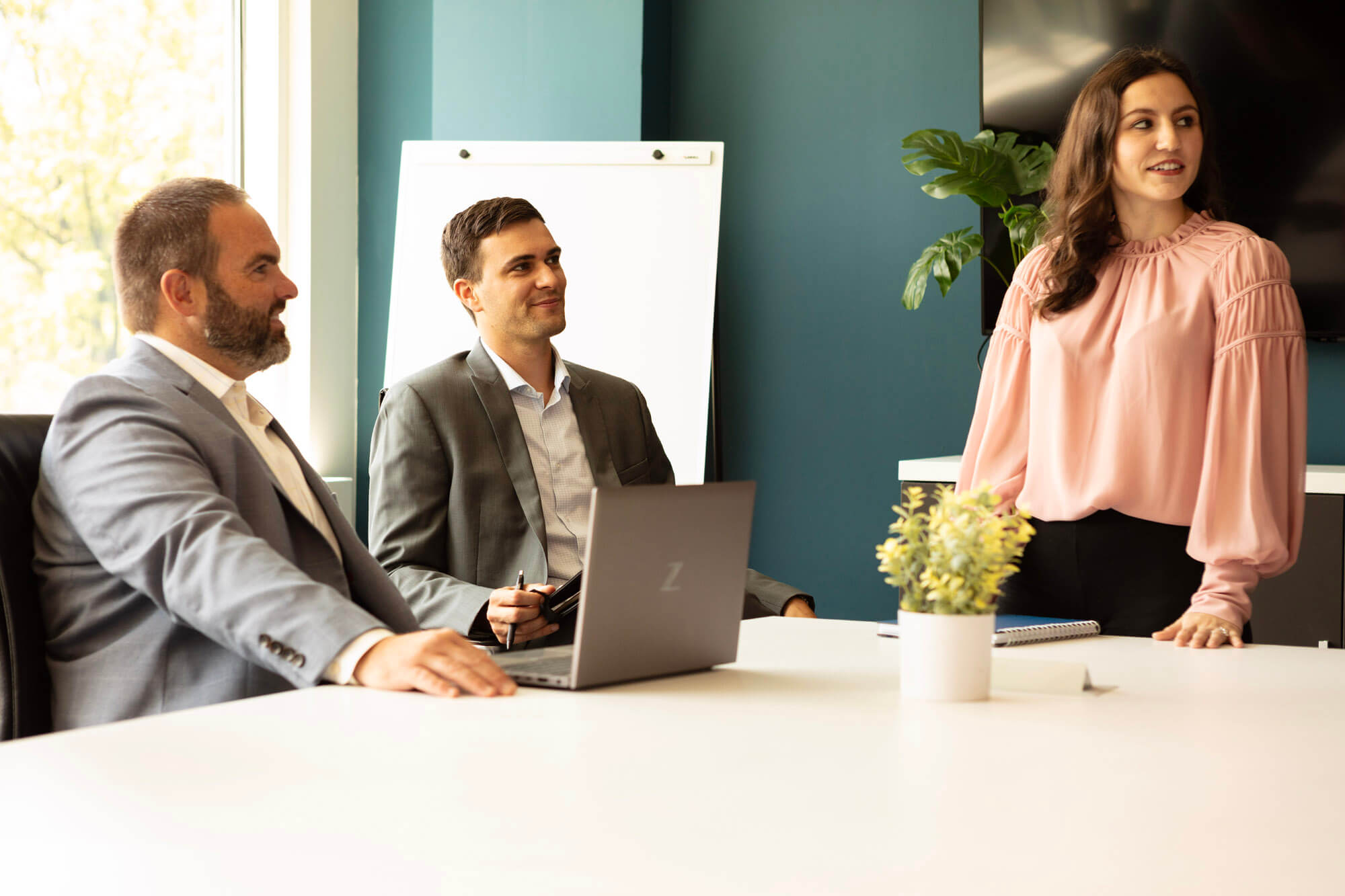 Two men sitting at a conference table and a woman standing at the table.