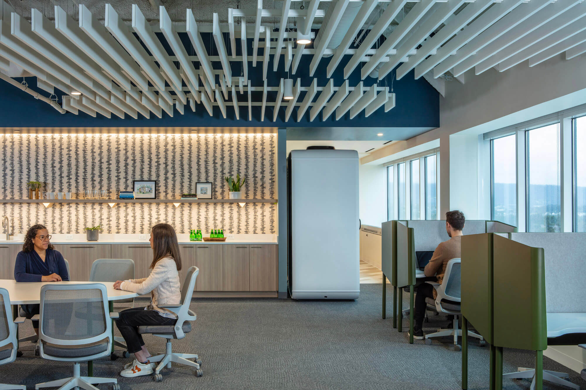 Image in a communal room within an office with three employees sitting at desks.