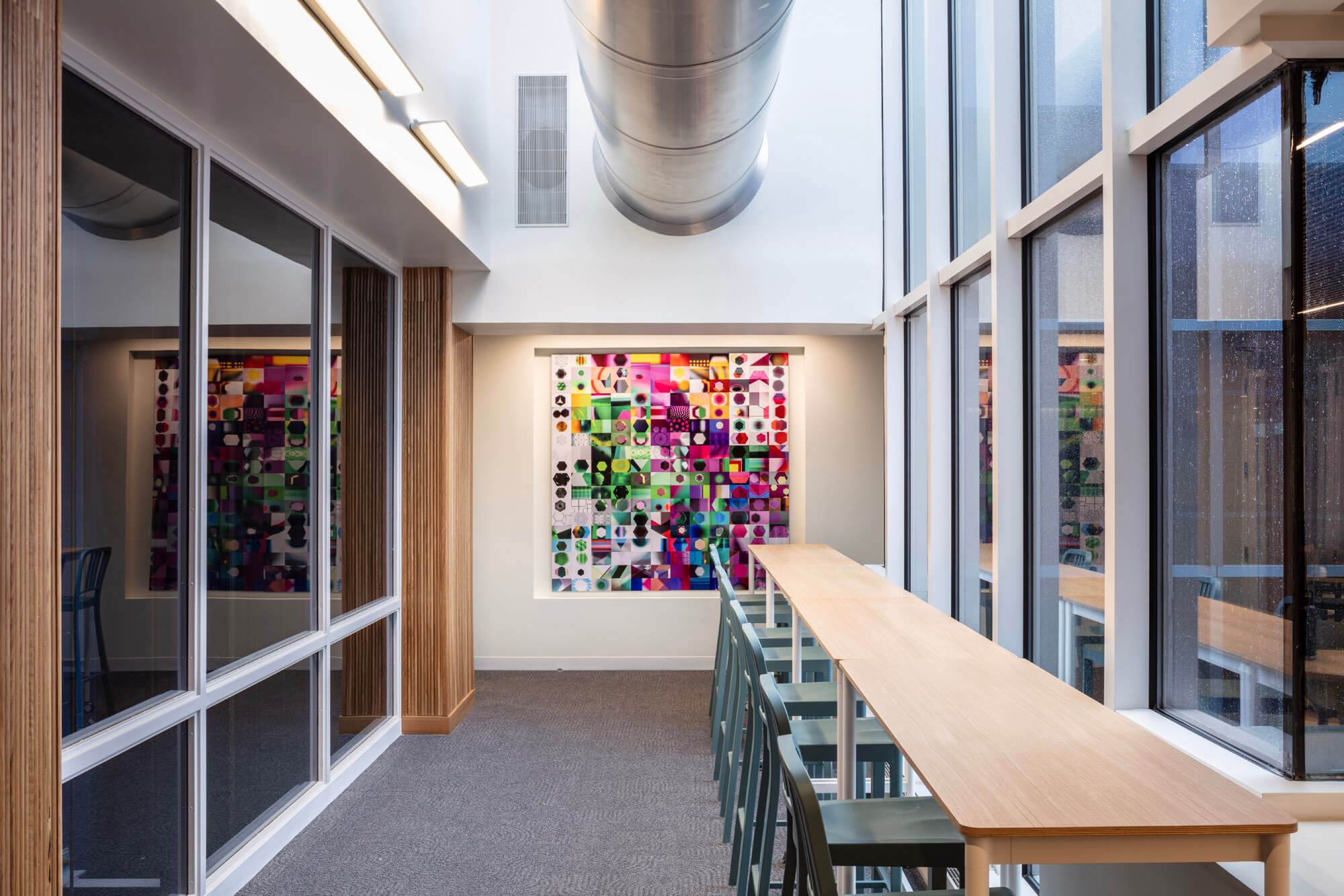 Looking along a long high top work space with blue chairs and a bright painting at the end of the area.