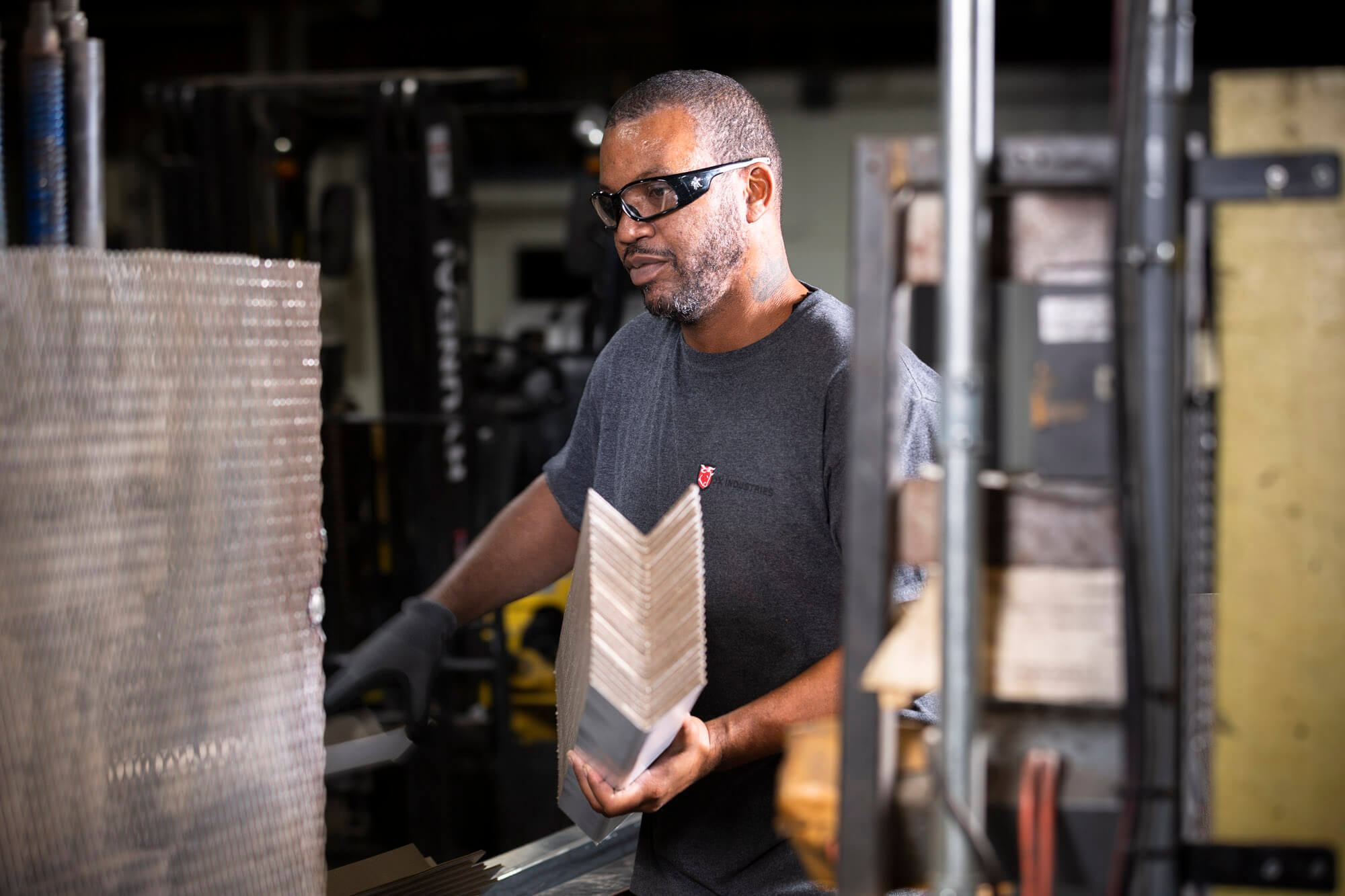 A man in safety glasses holding a stack of cardboard corners. He is in a factory.