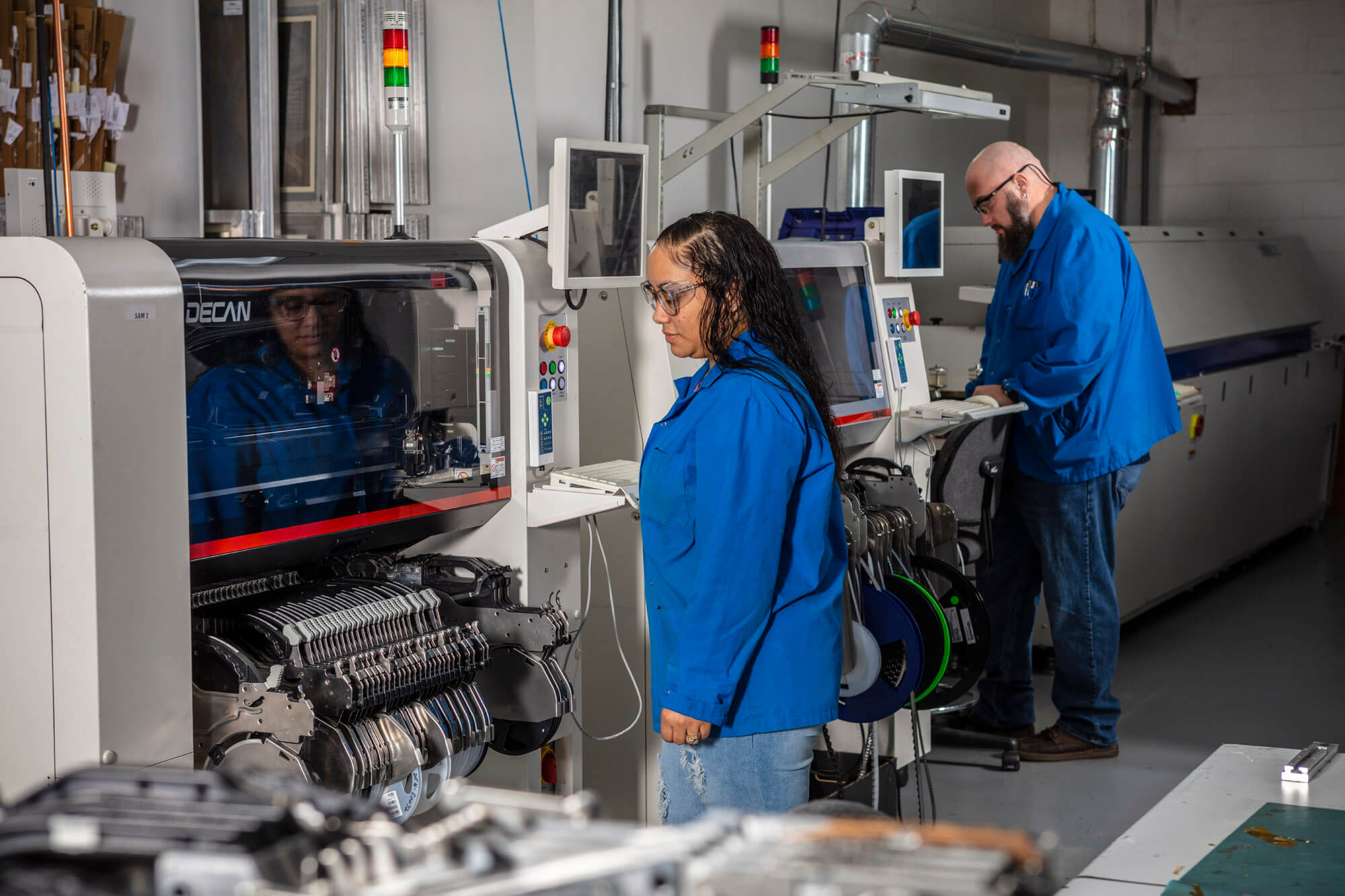 A man and woman standing in front of machinery, working to manufacture circuit boards.