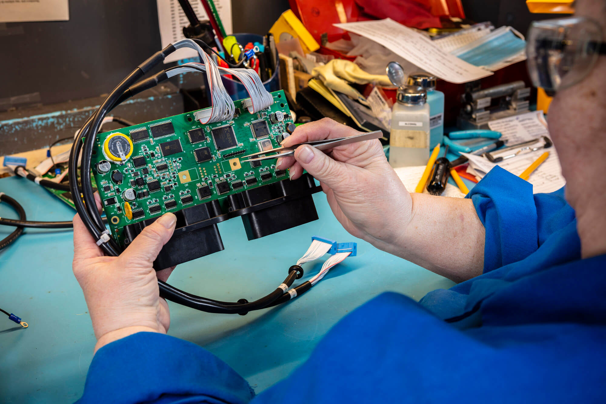 A women working with tweezers on a green circuit board.