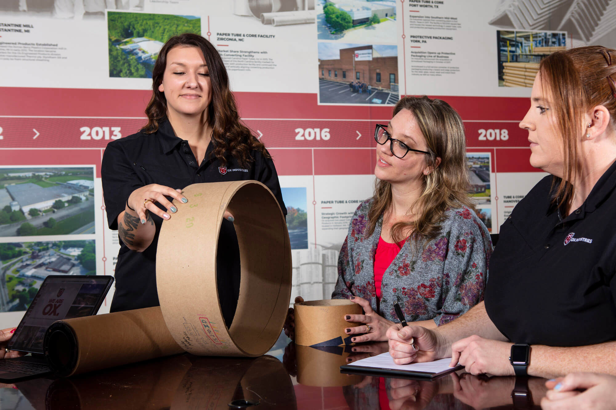 Three people talking and looking at a large carboard cylinder.