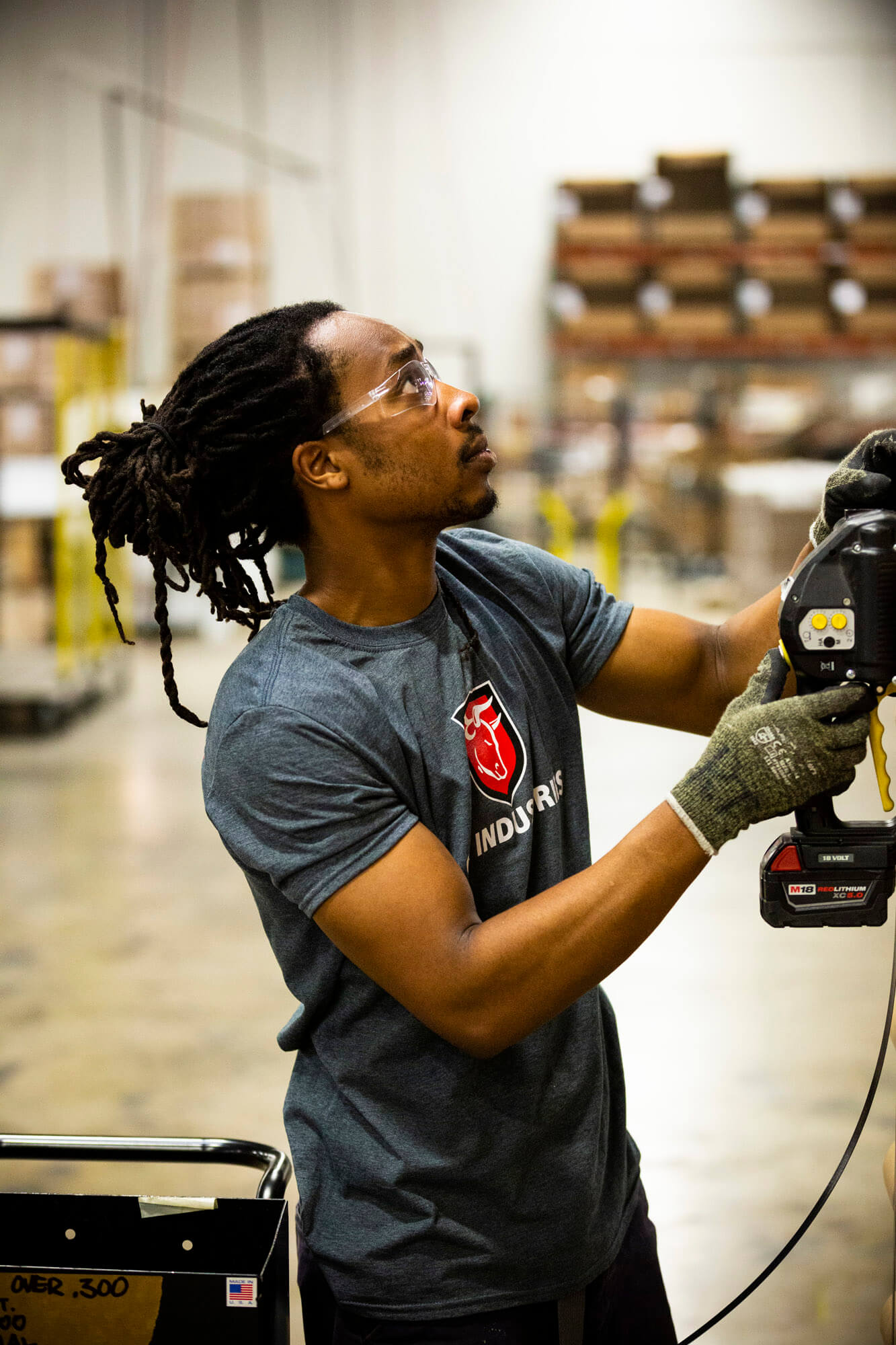 A man wearing an ox industries t-shirt is holding a piece of machinery in his hands.