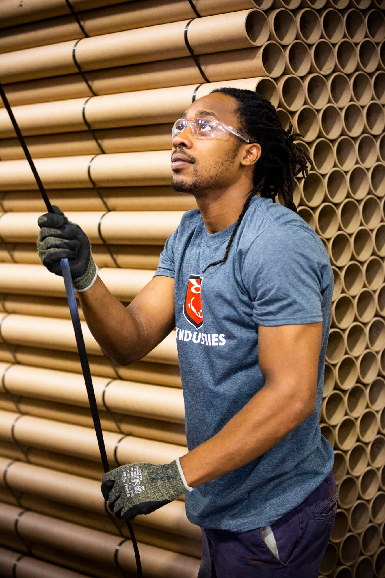 A man looking up and holding a black cable. He has a large stack of cardboard rolls behind him.