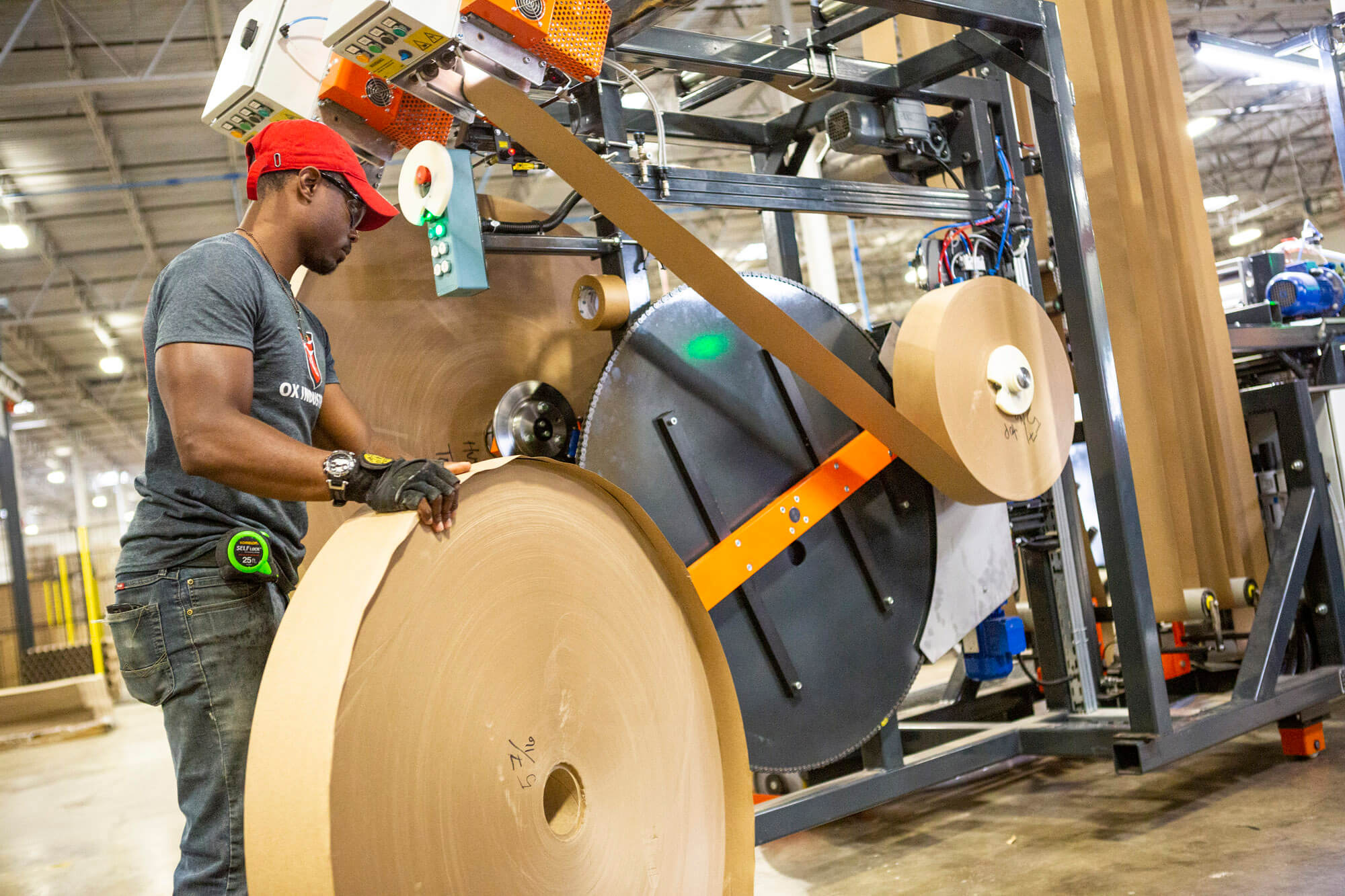 Man in a factory holding a large roll of cardboard.