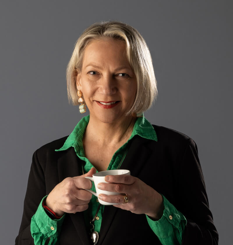 Woman standing looking at the camera with a cup of coffee in her hand.