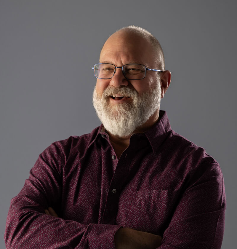 Man in a buttoned up shirt smiling at the camera.