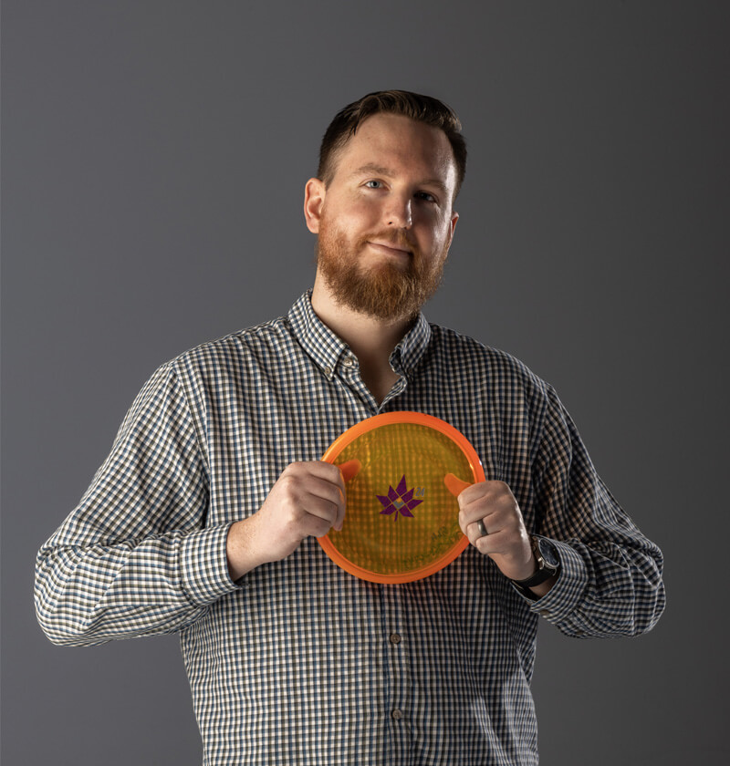 A man holding a disk for disk golf in front of his chest.