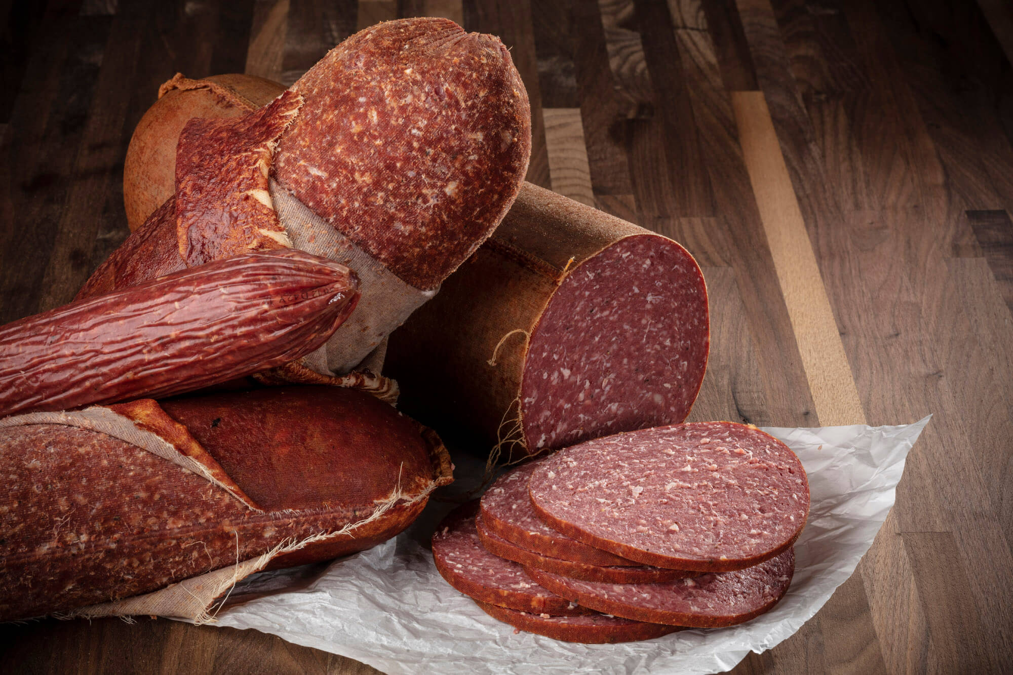 Four salami knobs of different sizes and several slices laying in front.