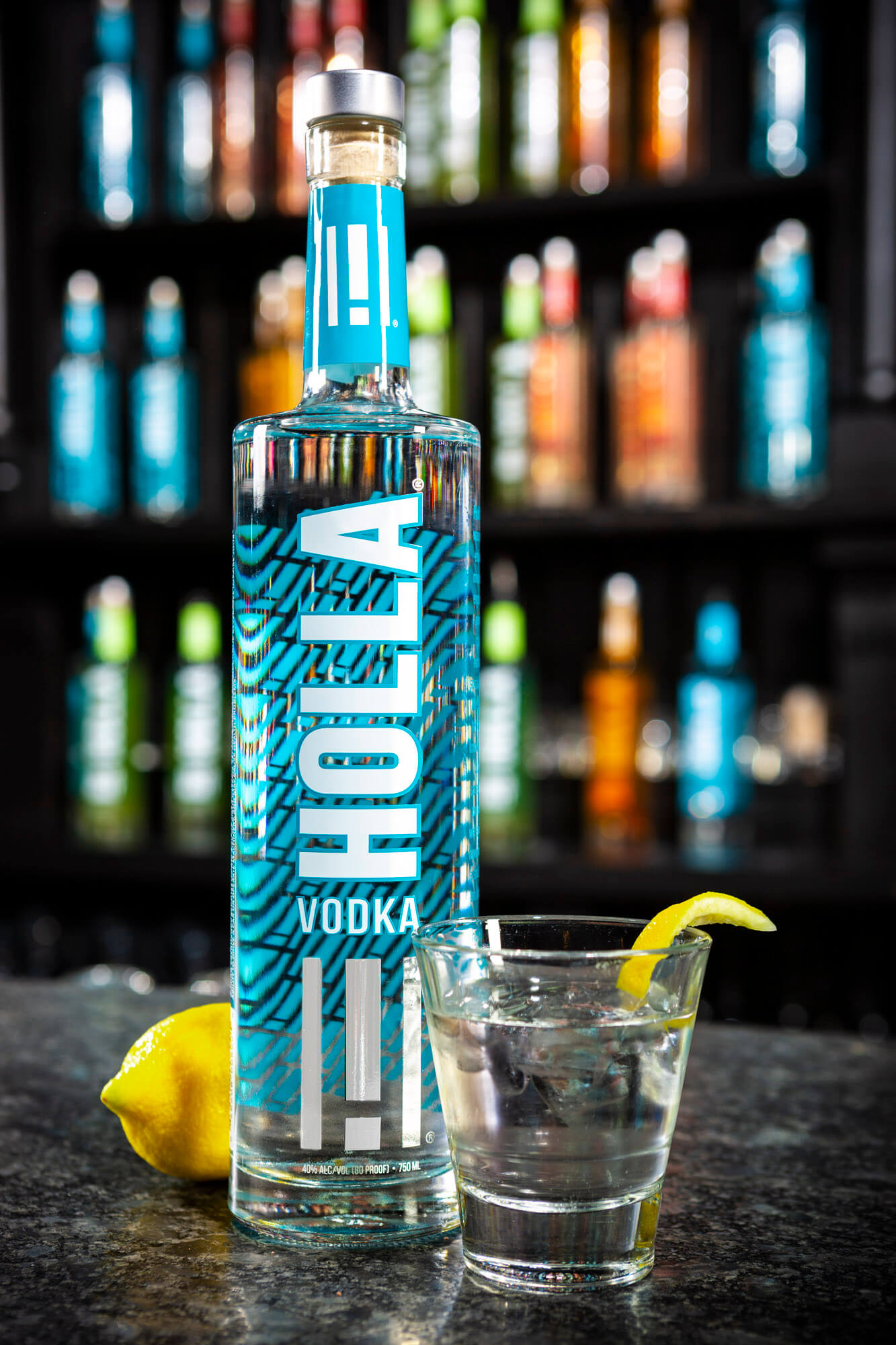 A bottle of vodka with a glass in front containing the drink and a piece of lemon.