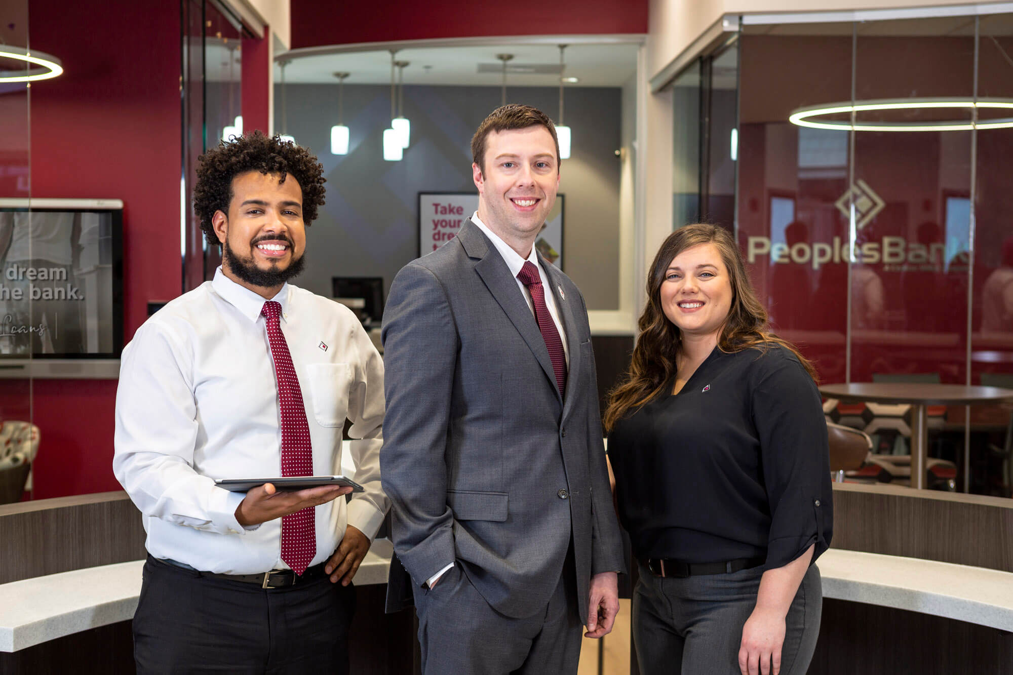 Three people standing in front of a desk and there is a glass office in the back ground.