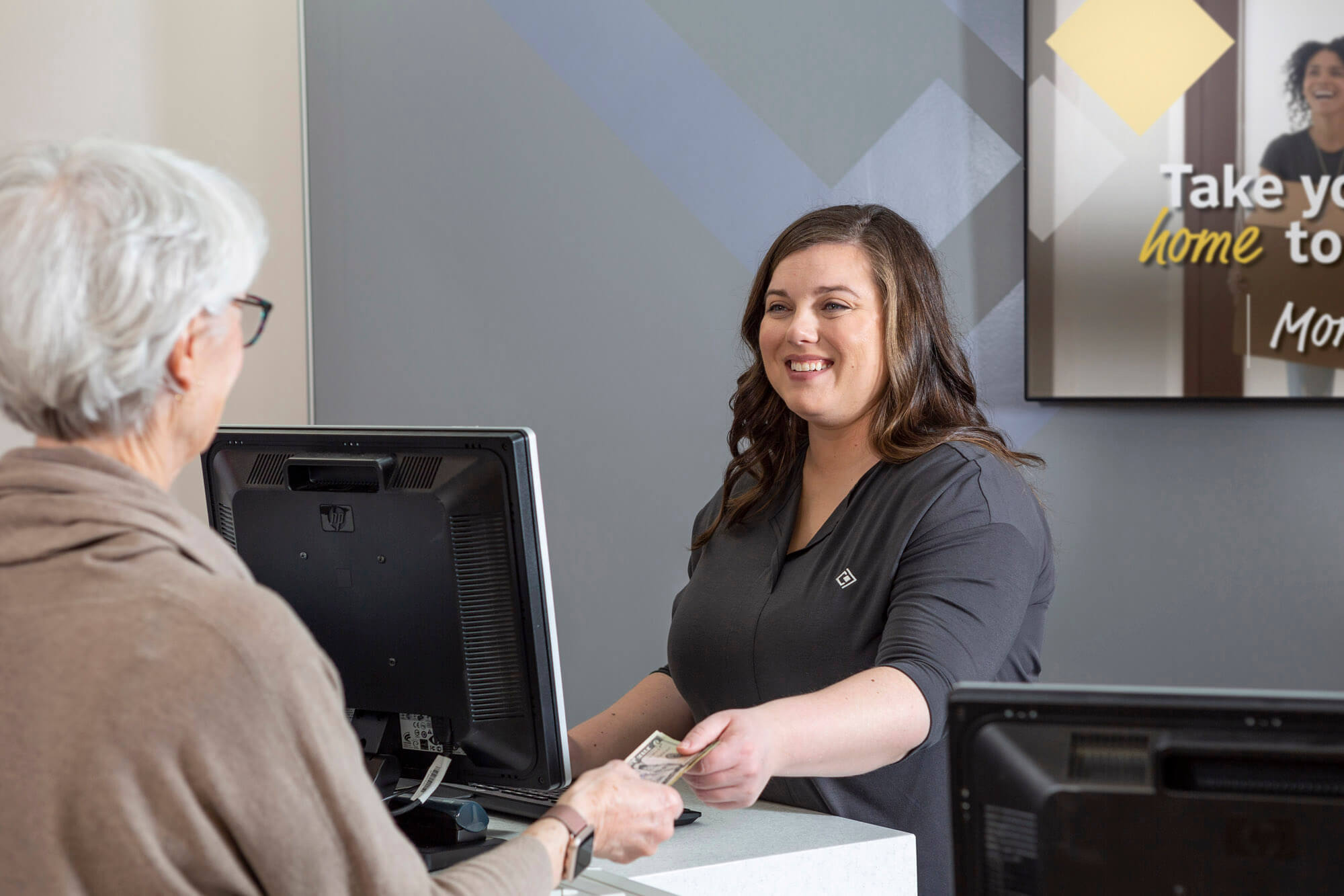 A smiling bank officer behind a desk handing a woman some money.