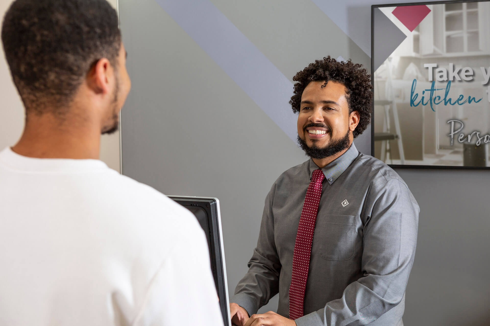 A man smiling from behind a computer screen to a customer.