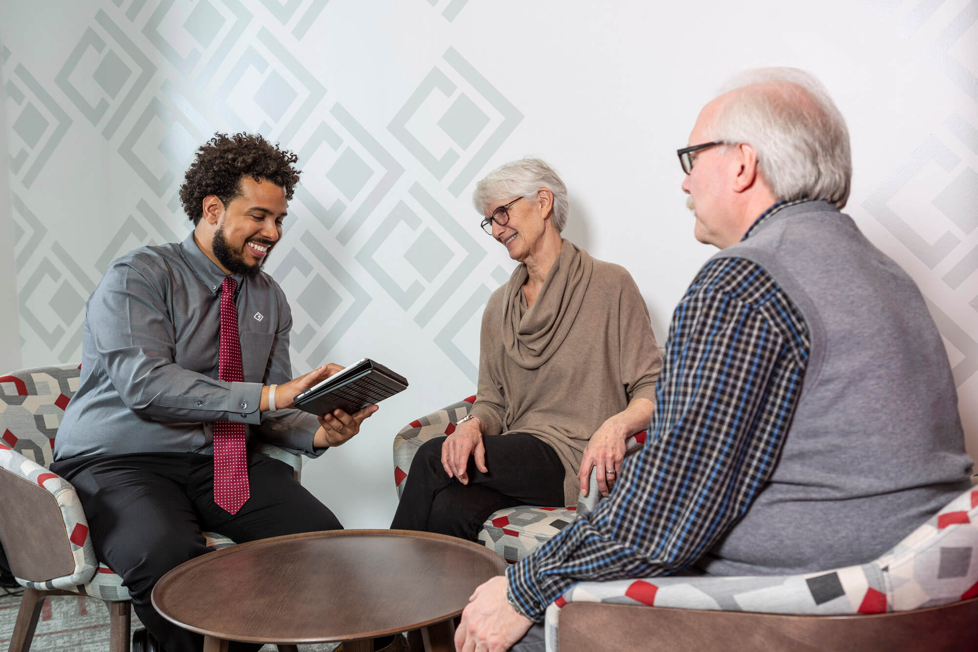 A bank officer showing an older woman and man something on his iPad while sitting at a desk.