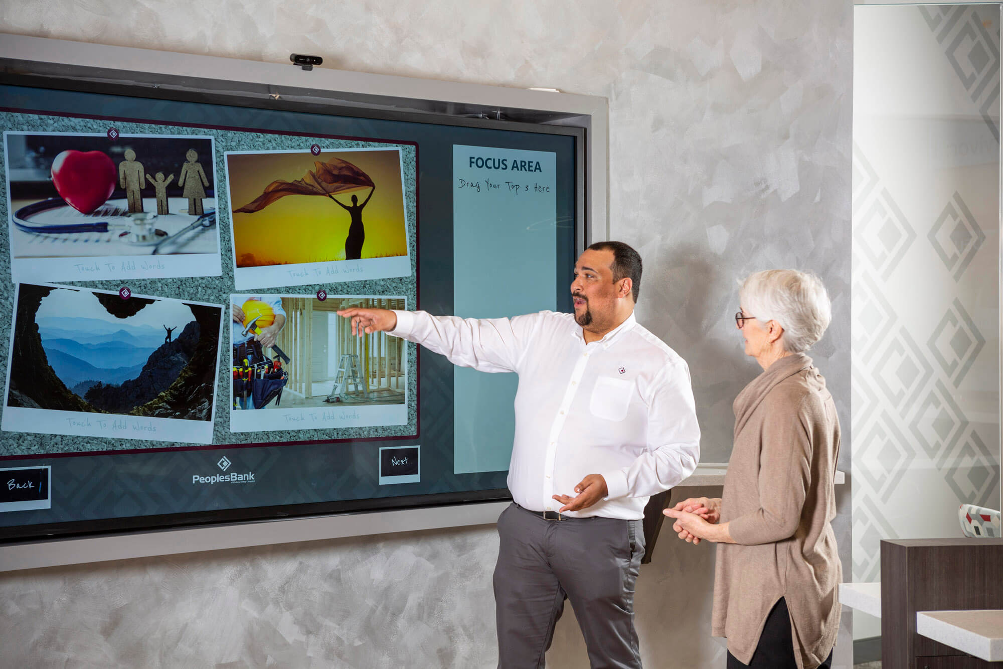 A man pointing to a large screen and a woman looking.