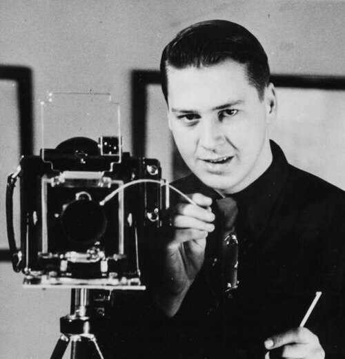 Black and white image of a man behind an old fashioned camera.