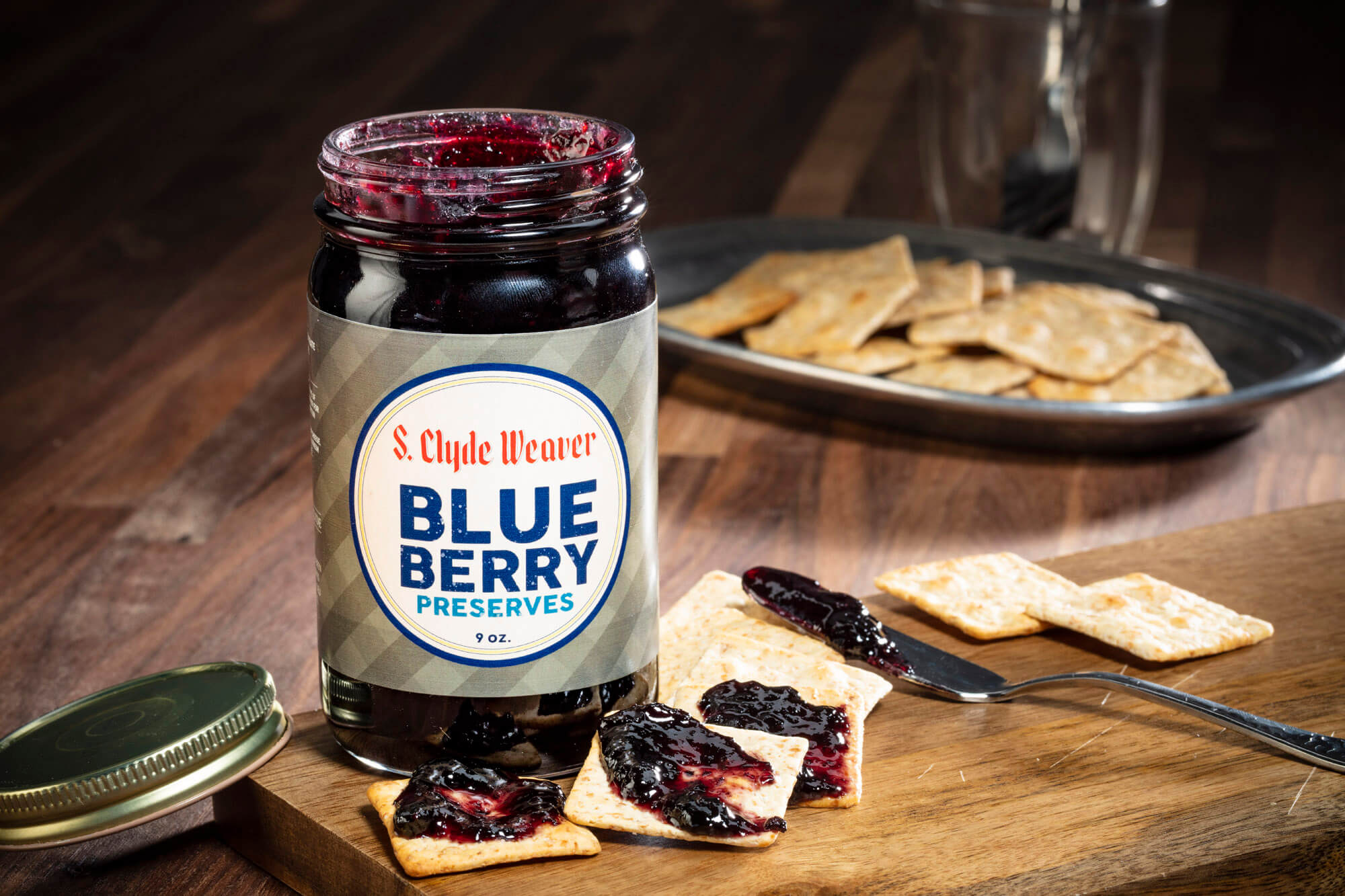 Close up jar of jam and crackers with jam on a wooden board.