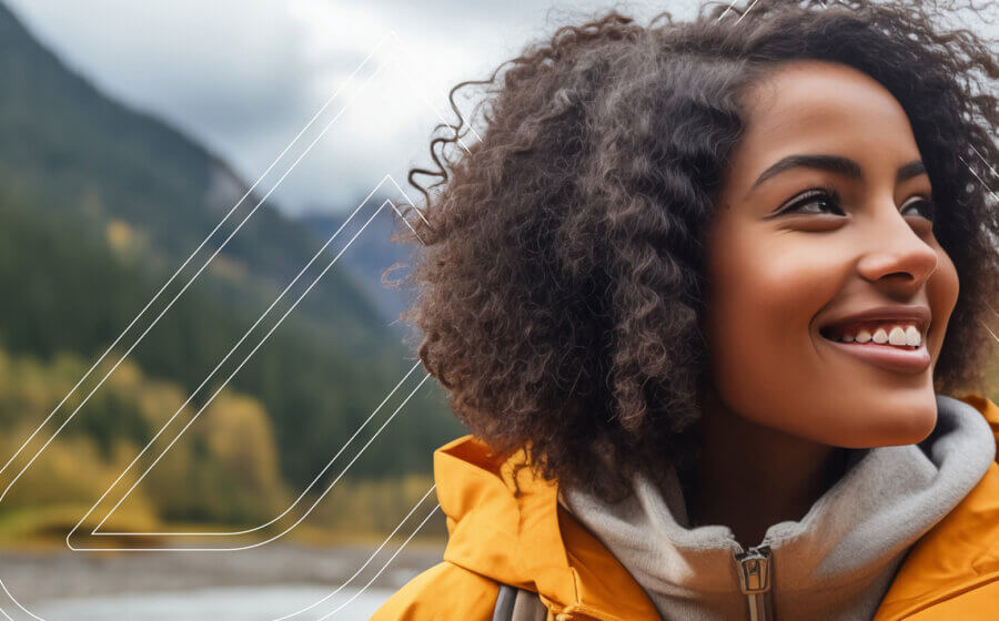 A girl in a yellow jacket looking to the side with mountains in the background.