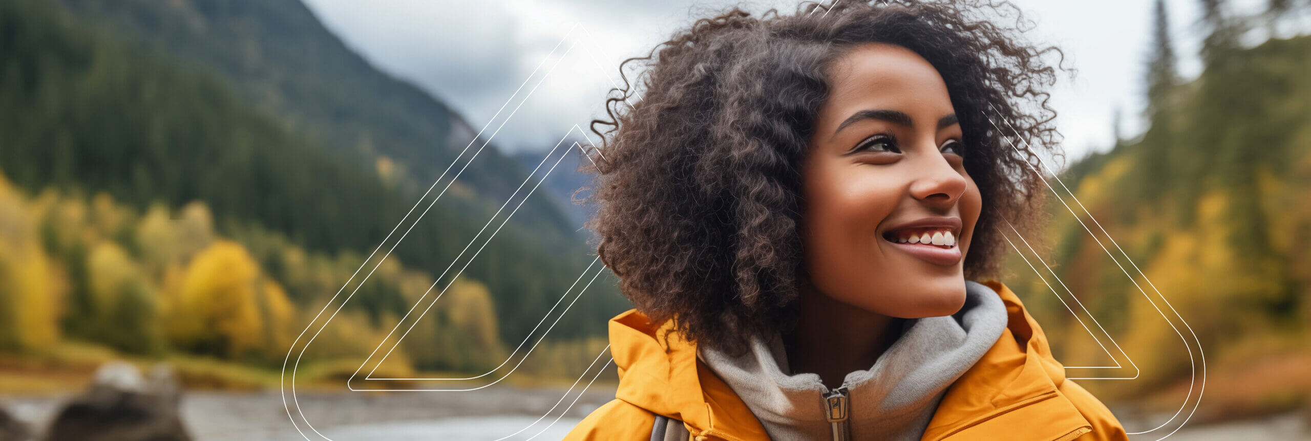 A girl in a yellow jacket looking to the side with mountains in the background.