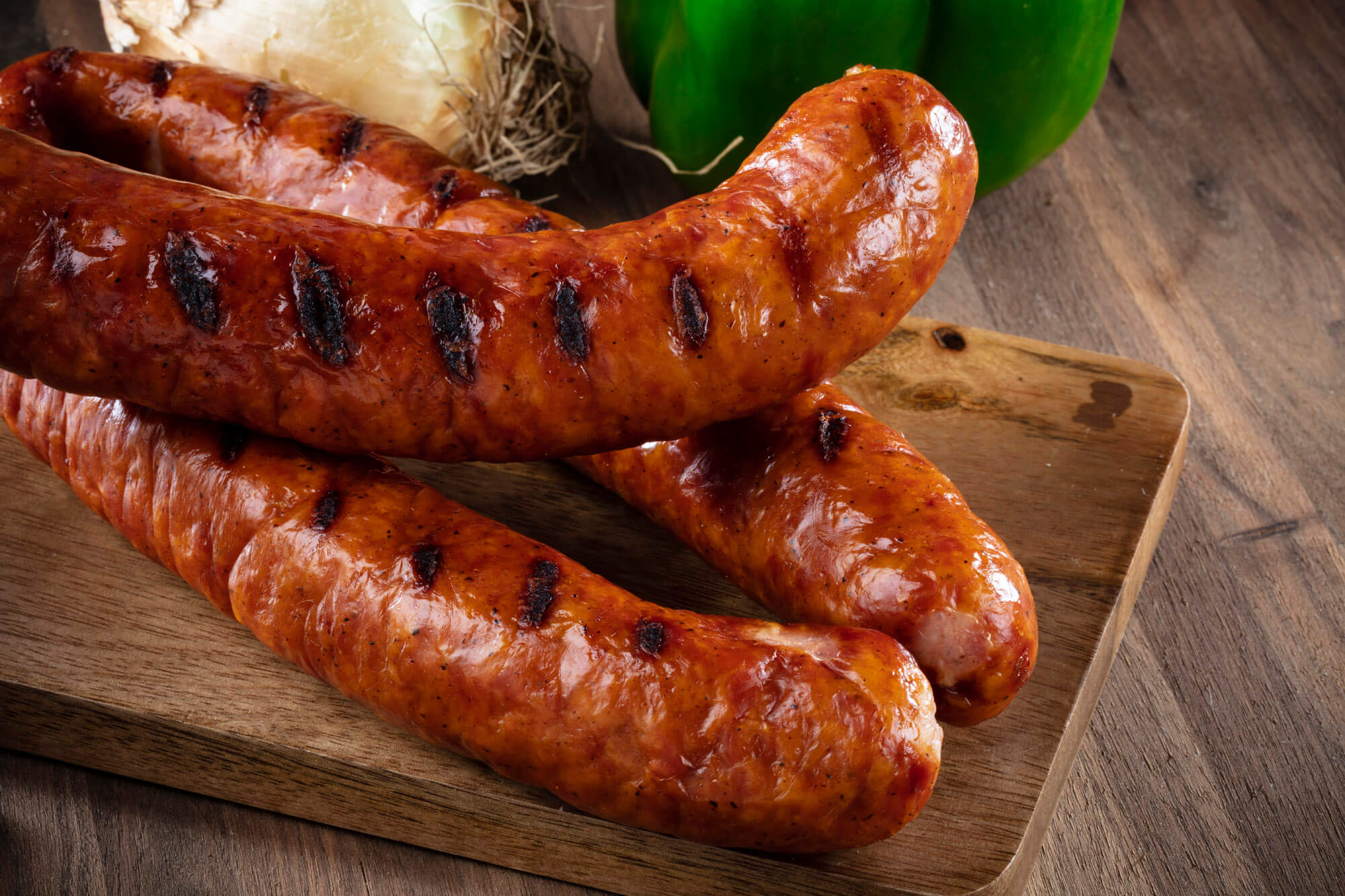 Three cooked sausages on a wooden board.