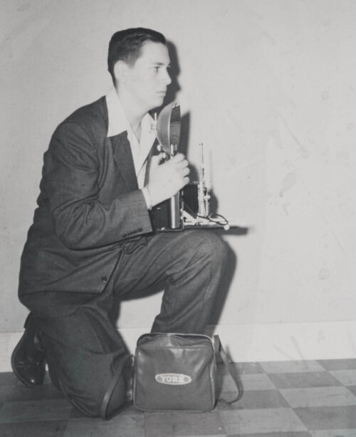 Old image of Jim Hayman kneeling on the floor with his camera at the ready.