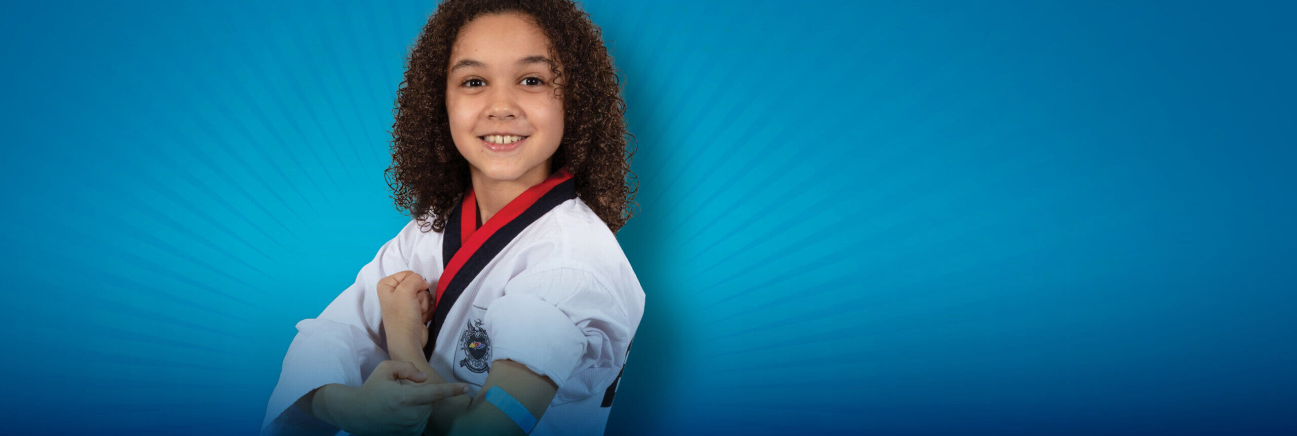 A young girl wearing her karate uniform and pointing to her arm where there is a band-aid.